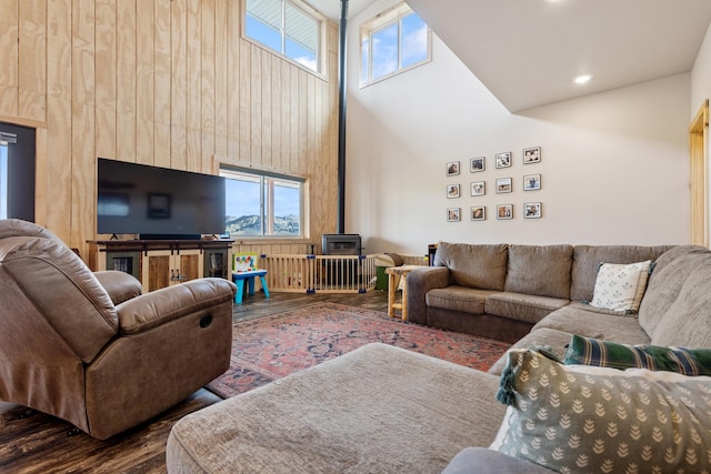 living room with wood walls, dark wood-type flooring, a towering ceiling, and a wood stove