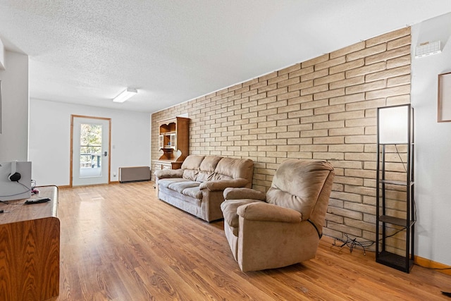 living room featuring brick wall, a textured ceiling, and light wood-type flooring