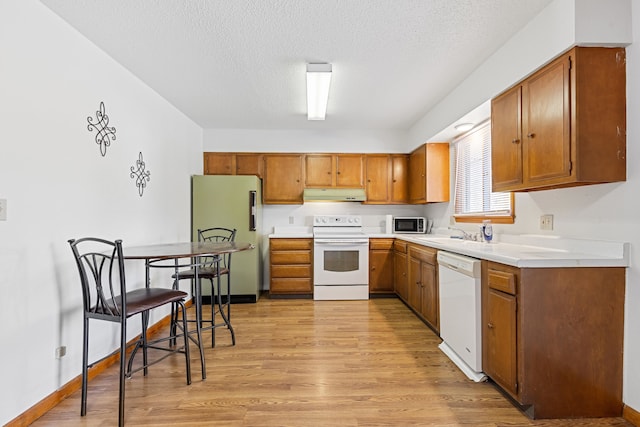 kitchen featuring a textured ceiling, sink, light wood-type flooring, and white appliances