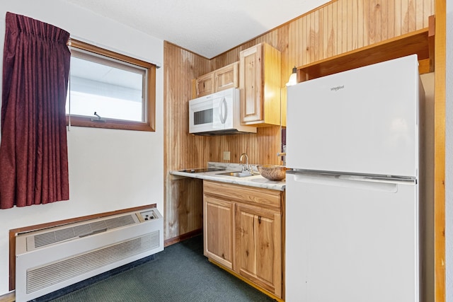 kitchen with dark carpet, wooden walls, sink, light brown cabinetry, and white appliances