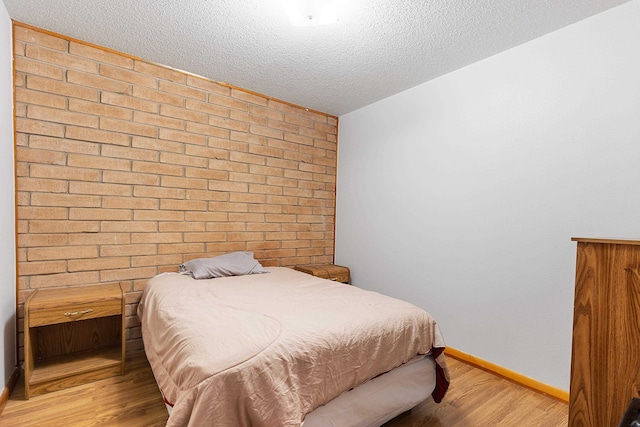 bedroom featuring brick wall, a textured ceiling, and light hardwood / wood-style floors