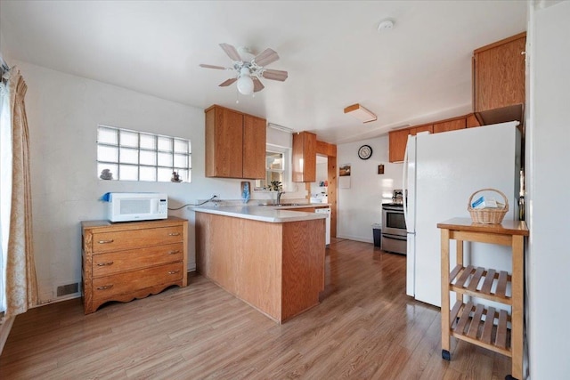 kitchen featuring white appliances, a peninsula, brown cabinetry, light wood finished floors, and light countertops