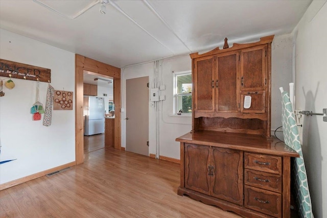 kitchen featuring freestanding refrigerator, light wood-style floors, brown cabinets, and baseboards