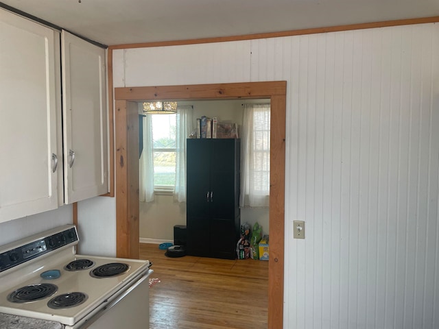 kitchen with white cabinetry, light wood-type flooring, wooden walls, and white range with electric stovetop