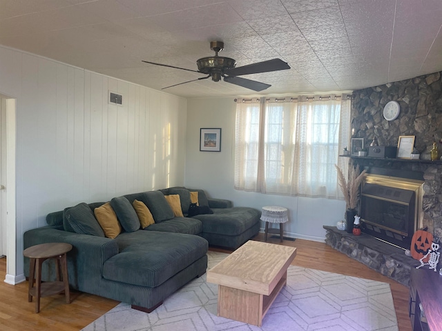 living room with wooden walls, hardwood / wood-style floors, ceiling fan, and a fireplace