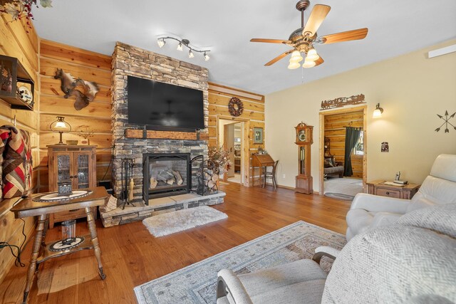 living room with a stone fireplace, wooden walls, wood-type flooring, and ceiling fan