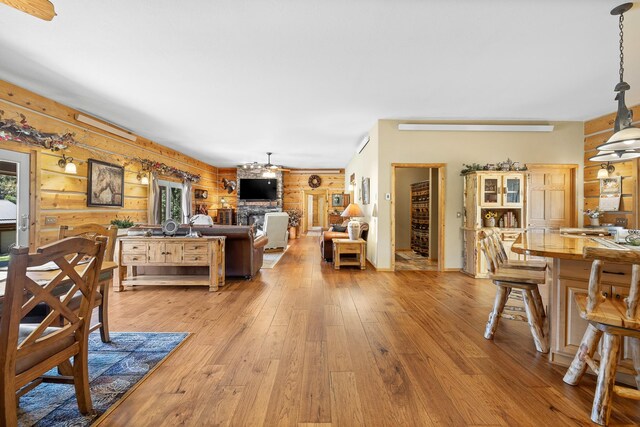 dining room with light wood-type flooring, wooden walls, ceiling fan, and a large fireplace