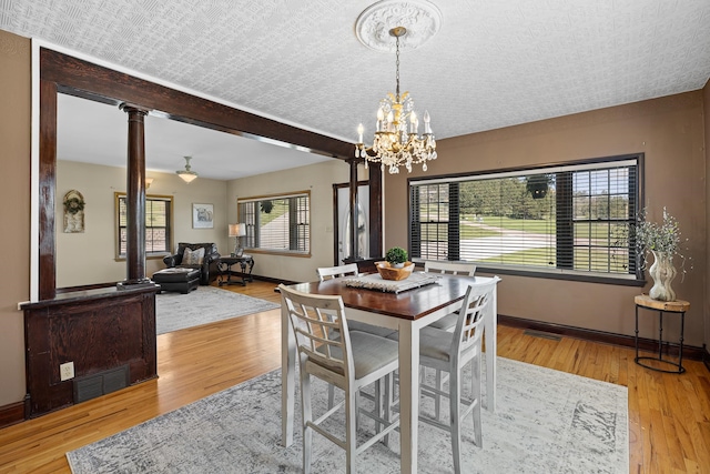 dining room with ornate columns, an inviting chandelier, light hardwood / wood-style floors, and a textured ceiling