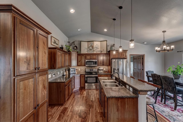 kitchen featuring stainless steel appliances, hanging light fixtures, sink, lofted ceiling, and a kitchen island with sink