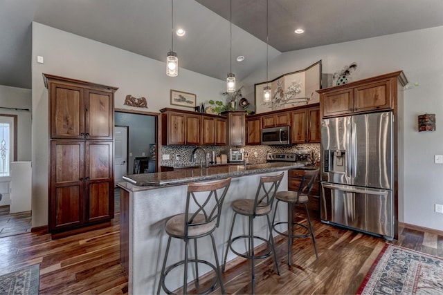 kitchen with pendant lighting, appliances with stainless steel finishes, dark wood-type flooring, and a center island with sink