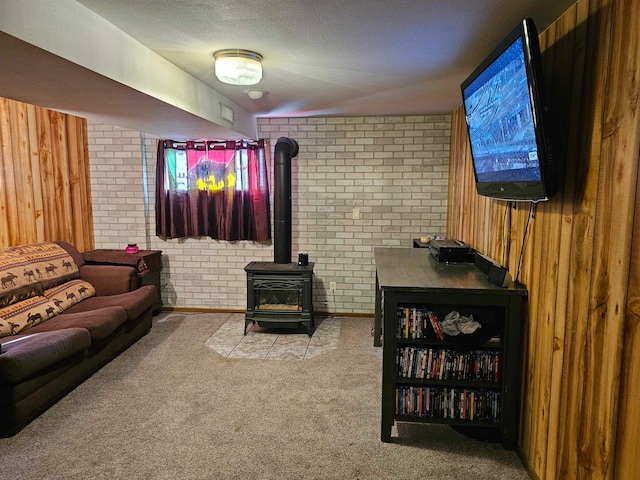 carpeted living room with wooden walls, a wood stove, a textured ceiling, and brick wall