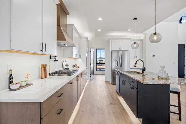 kitchen with wall chimney exhaust hood, sink, pendant lighting, a large island with sink, and white cabinetry