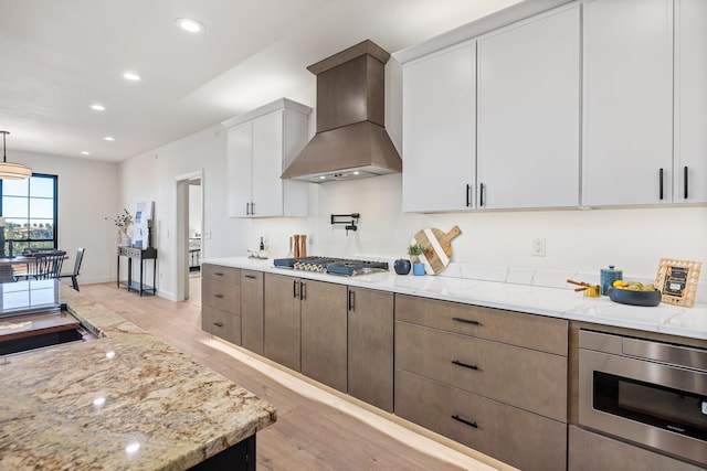 kitchen with light stone counters, custom range hood, light hardwood / wood-style flooring, white cabinetry, and stainless steel gas stovetop