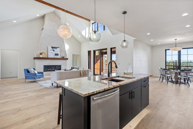 kitchen featuring a large fireplace, dishwasher, sink, an island with sink, and pendant lighting