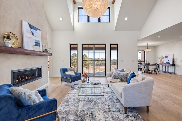 living room featuring a fireplace, a towering ceiling, a healthy amount of sunlight, and light hardwood / wood-style floors