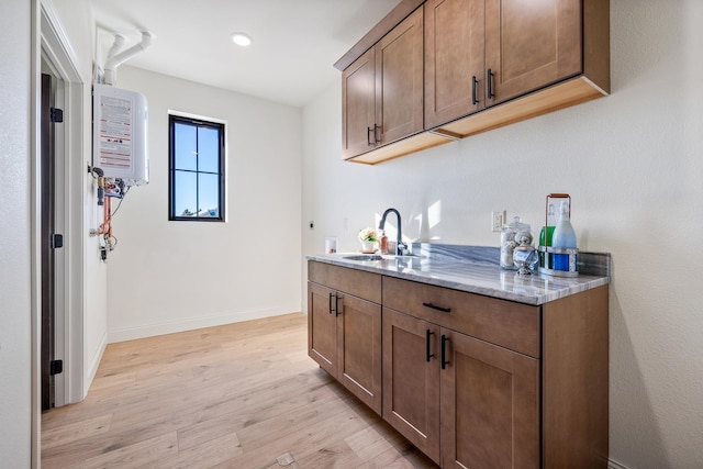 kitchen featuring light hardwood / wood-style floors, light stone counters, sink, and water heater