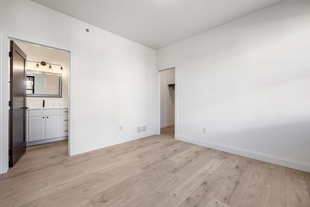 unfurnished bedroom featuring a walk in closet, light hardwood / wood-style floors, and ensuite bath