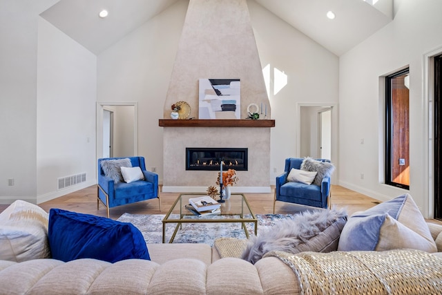 living room with light wood-type flooring, a large fireplace, and high vaulted ceiling