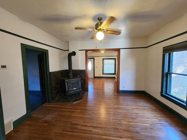 unfurnished living room with a textured ceiling, a wood stove, ceiling fan, and dark wood-type flooring