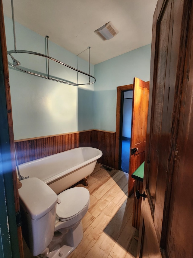 bathroom featuring wood-type flooring, toilet, a tub, and wood walls