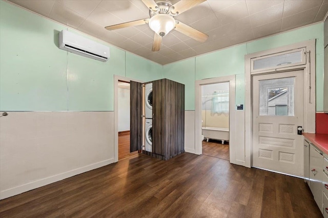 unfurnished bedroom with a wall mounted air conditioner, dark hardwood / wood-style flooring, ensuite bath, ceiling fan, and stacked washer / dryer