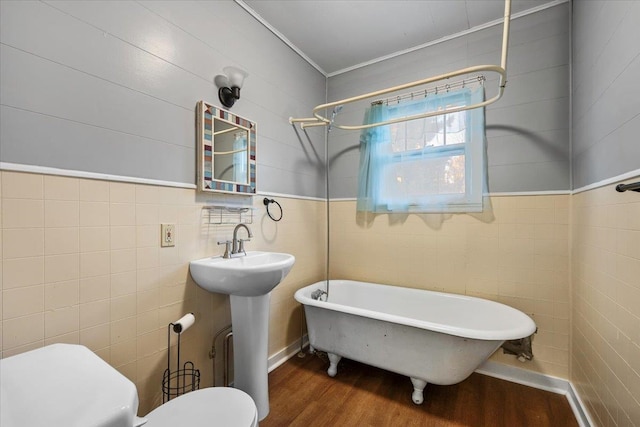 bathroom with hardwood / wood-style floors, a bathtub, toilet, ornamental molding, and tile walls