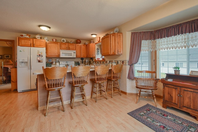 kitchen featuring a kitchen breakfast bar, white appliances, a textured ceiling, and light hardwood / wood-style flooring