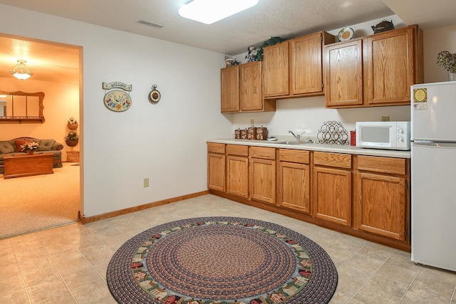 kitchen featuring a textured ceiling, white appliances, light colored carpet, and sink