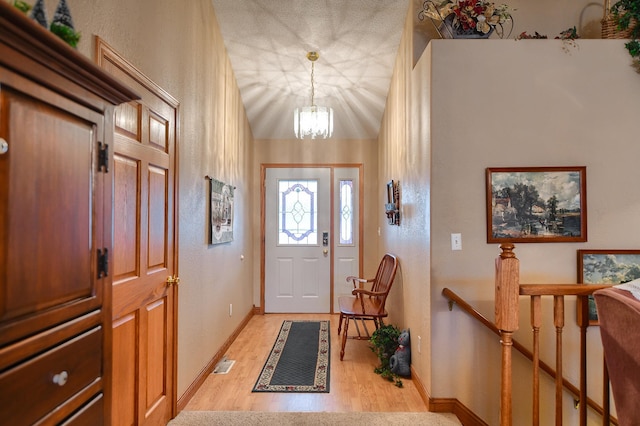 doorway to outside with lofted ceiling, light wood-type flooring, a textured ceiling, and a chandelier