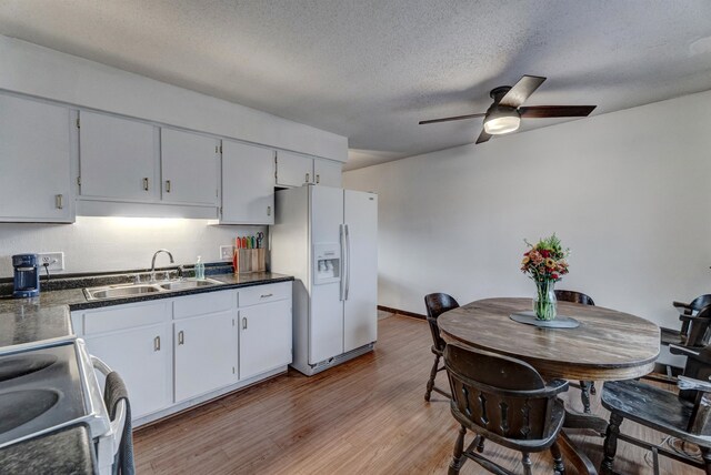 kitchen with a textured ceiling, sink, white refrigerator with ice dispenser, hardwood / wood-style flooring, and range