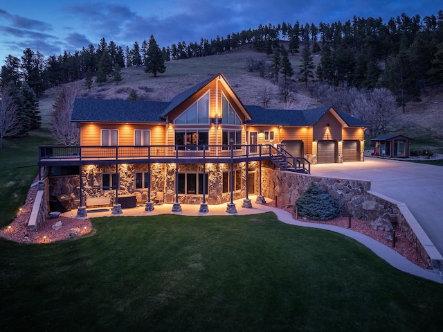 back house at dusk with a garage, a yard, and a wooden deck