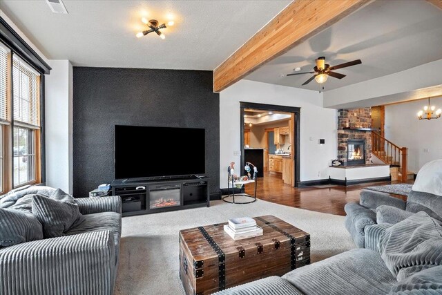 living room with beamed ceiling, ceiling fan with notable chandelier, a stone fireplace, and dark wood-type flooring