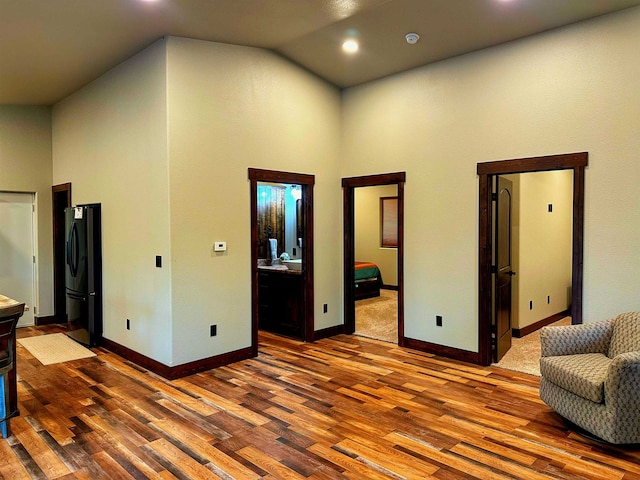 interior space with ensuite bathroom, black refrigerator, wood-type flooring, and high vaulted ceiling