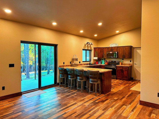 kitchen featuring kitchen peninsula, a breakfast bar, stainless steel appliances, dark wood-type flooring, and sink