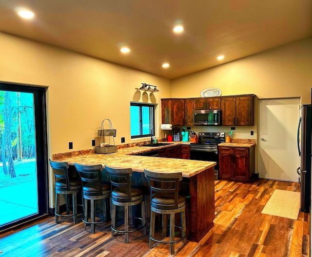 kitchen with sink, a kitchen breakfast bar, dark hardwood / wood-style flooring, kitchen peninsula, and appliances with stainless steel finishes