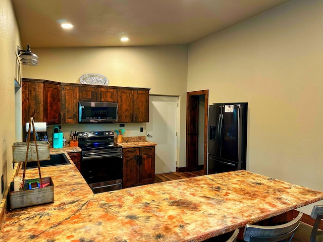 kitchen featuring stainless steel appliances, dark hardwood / wood-style flooring, kitchen peninsula, a breakfast bar area, and dark brown cabinets