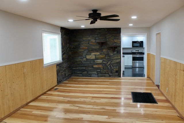 kitchen with stainless steel electric range oven, light hardwood / wood-style flooring, and wooden walls