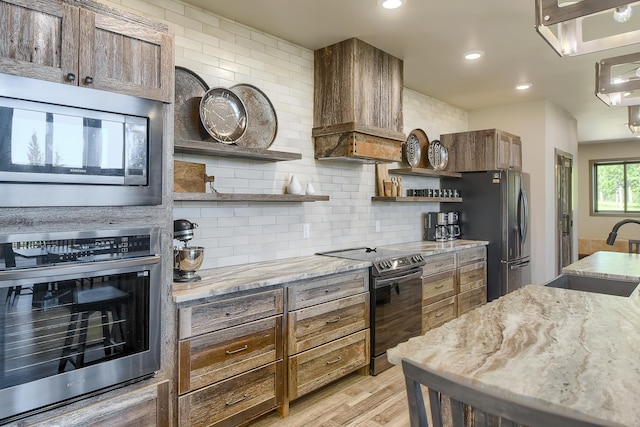 kitchen featuring light stone countertops, appliances with stainless steel finishes, custom range hood, sink, and light hardwood / wood-style flooring