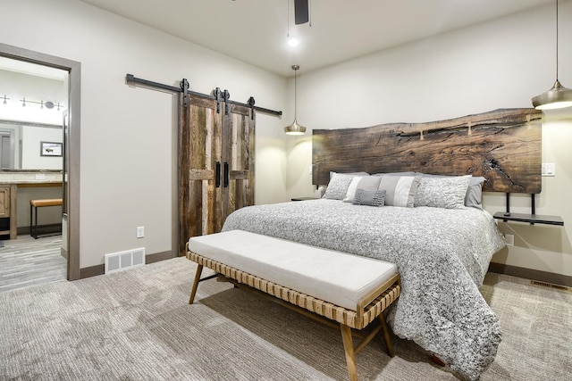 bedroom with carpet floors, a barn door, ceiling fan, and ensuite bath