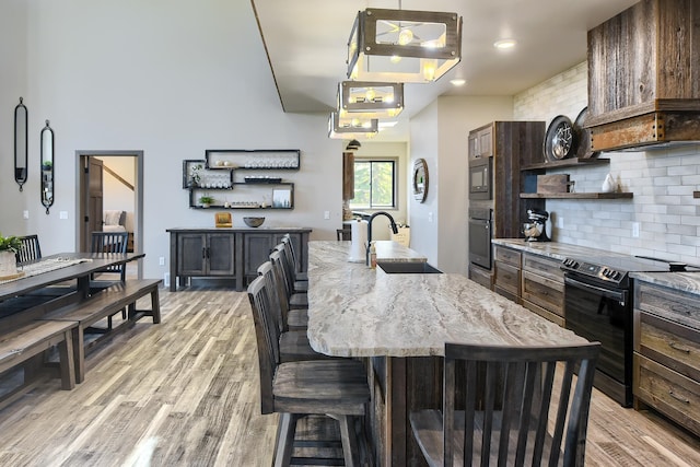 kitchen with hanging light fixtures, an island with sink, black appliances, and sink