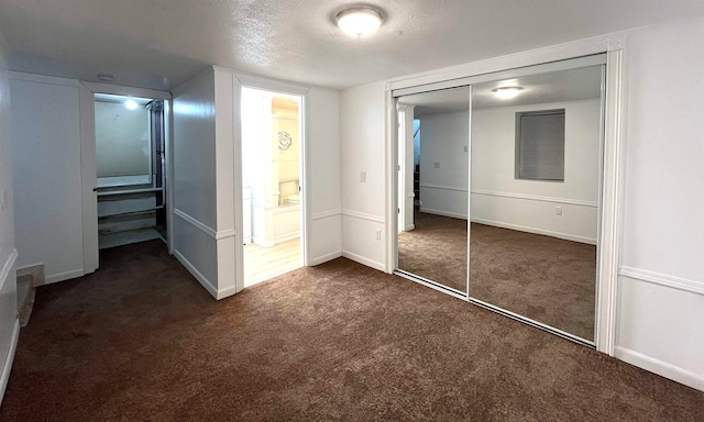 unfurnished bedroom with dark carpet, a textured ceiling, and a closet