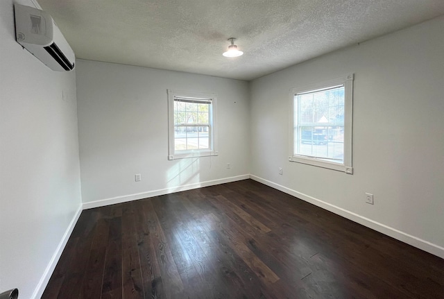 spare room featuring a wall unit AC, a wealth of natural light, dark hardwood / wood-style flooring, and a textured ceiling