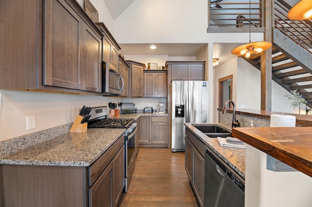 kitchen with light stone countertops, sink, stainless steel appliances, wood-type flooring, and decorative light fixtures