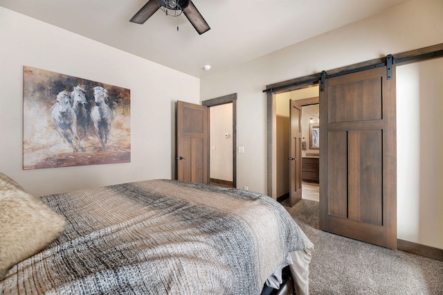 carpeted bedroom with a barn door, ceiling fan, and ensuite bath