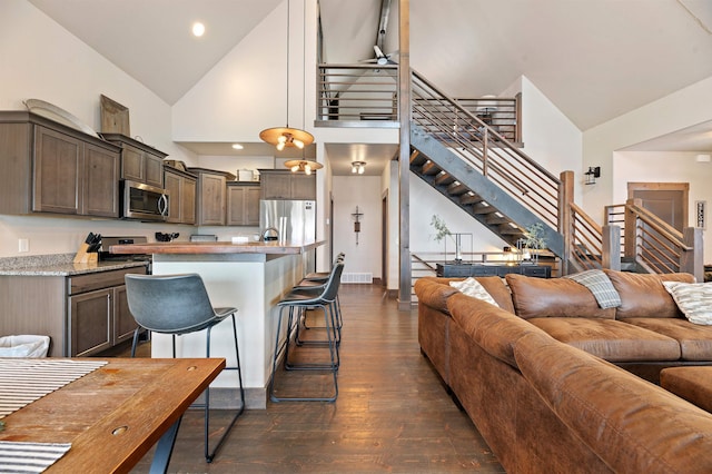 kitchen with stainless steel appliances, high vaulted ceiling, dark hardwood / wood-style floors, hanging light fixtures, and an island with sink