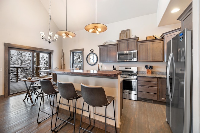 kitchen with stainless steel appliances, dark wood-type flooring, a center island with sink, a notable chandelier, and hanging light fixtures