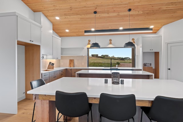 kitchen featuring vaulted ceiling, pendant lighting, wooden ceiling, light hardwood / wood-style floors, and white cabinetry