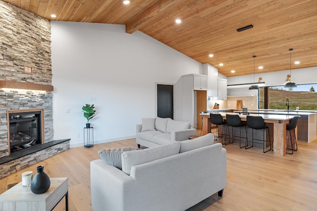 living room featuring beam ceiling, a stone fireplace, high vaulted ceiling, and light hardwood / wood-style flooring