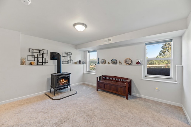 living area featuring light carpet, a wood stove, and a healthy amount of sunlight