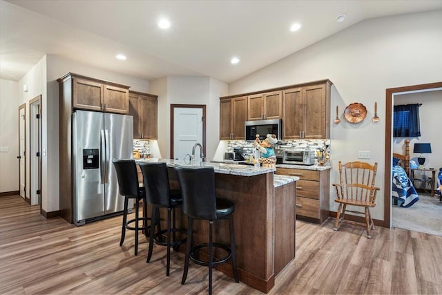 kitchen featuring appliances with stainless steel finishes, backsplash, a kitchen island with sink, light hardwood / wood-style flooring, and lofted ceiling